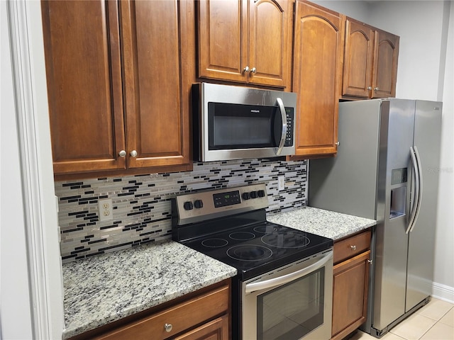 kitchen featuring decorative backsplash, appliances with stainless steel finishes, light tile patterned floors, and light stone counters