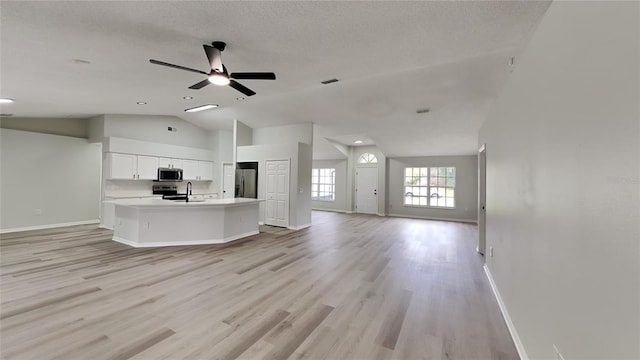 unfurnished living room featuring ceiling fan, sink, light hardwood / wood-style flooring, a textured ceiling, and vaulted ceiling