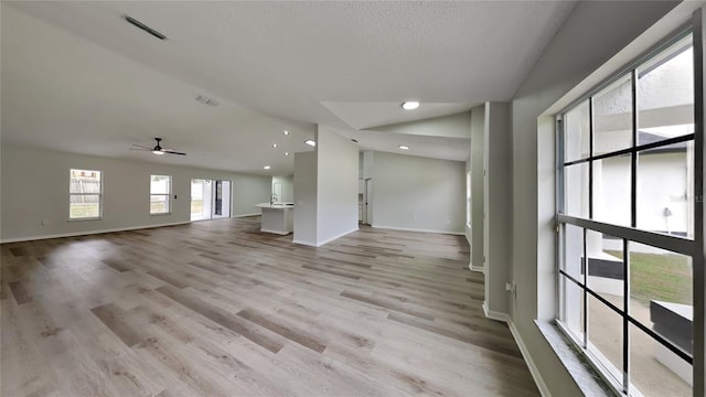 unfurnished living room featuring a textured ceiling, ceiling fan, light hardwood / wood-style flooring, and vaulted ceiling