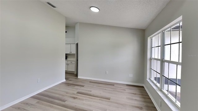 spare room with a textured ceiling, light hardwood / wood-style flooring, and a wealth of natural light