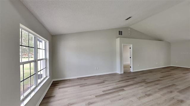 unfurnished room with a textured ceiling, light hardwood / wood-style floors, and lofted ceiling