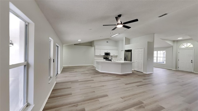 unfurnished living room with ceiling fan, sink, light hardwood / wood-style flooring, a textured ceiling, and vaulted ceiling