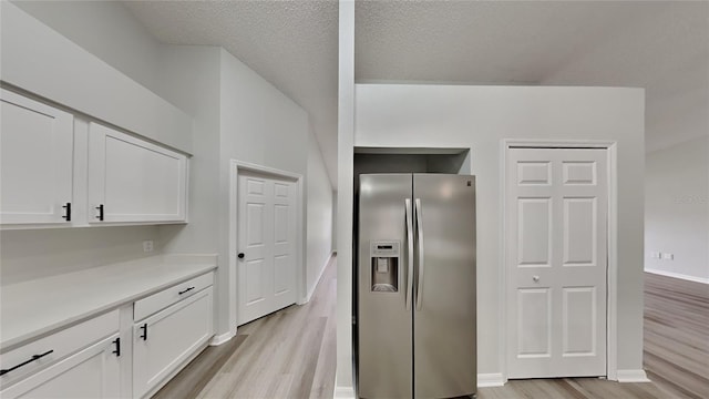 kitchen with white cabinets, stainless steel fridge, a textured ceiling, and light hardwood / wood-style flooring