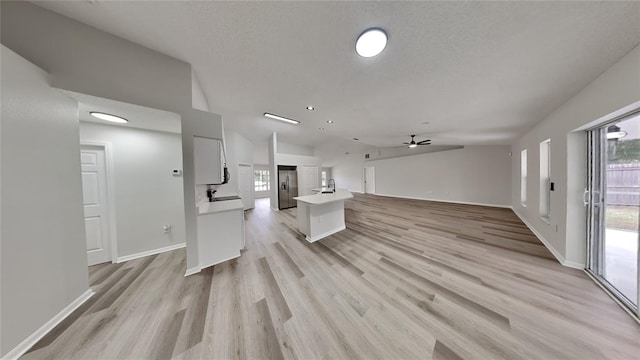 unfurnished living room with lofted ceiling, sink, ceiling fan, a textured ceiling, and light hardwood / wood-style floors