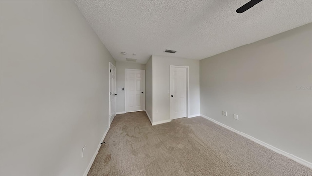 unfurnished bedroom featuring ceiling fan, light carpet, and a textured ceiling