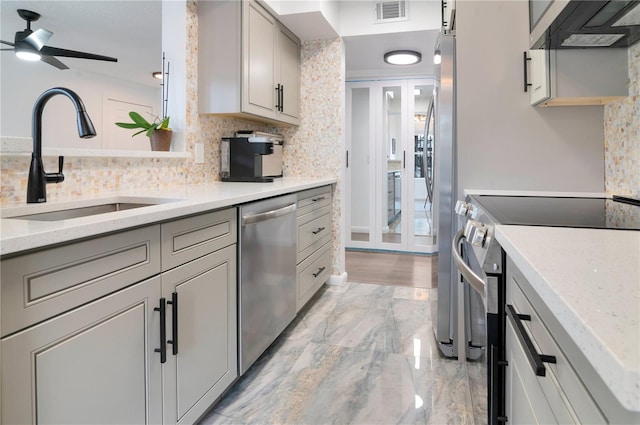 kitchen with wall chimney range hood, sink, ceiling fan, light stone countertops, and appliances with stainless steel finishes