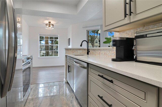 kitchen with light stone countertops, appliances with stainless steel finishes, plenty of natural light, and sink