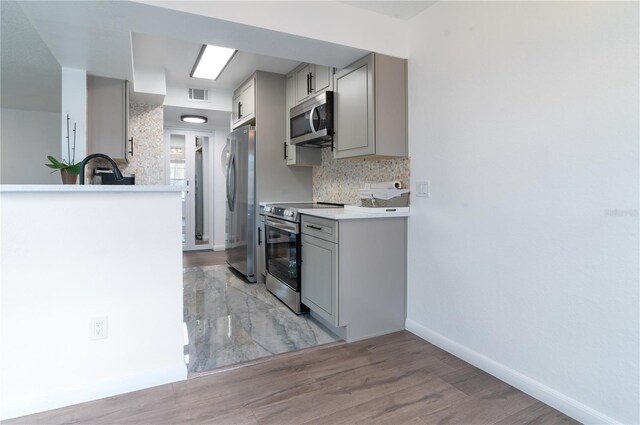 kitchen with gray cabinetry, light wood-type flooring, stainless steel appliances, and tasteful backsplash