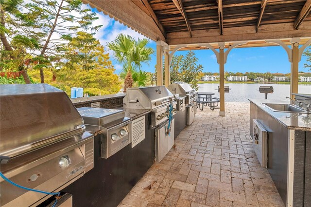 view of patio / terrace featuring a grill, a water view, exterior kitchen, and sink