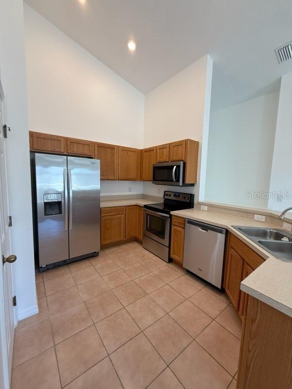 kitchen with high vaulted ceiling, sink, light tile patterned flooring, kitchen peninsula, and stainless steel appliances