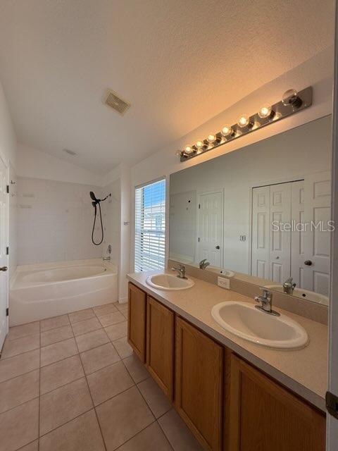 bathroom featuring vanity, a bath, vaulted ceiling, tile patterned flooring, and a textured ceiling