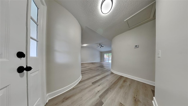 hallway with a textured ceiling, light hardwood / wood-style flooring, and vaulted ceiling