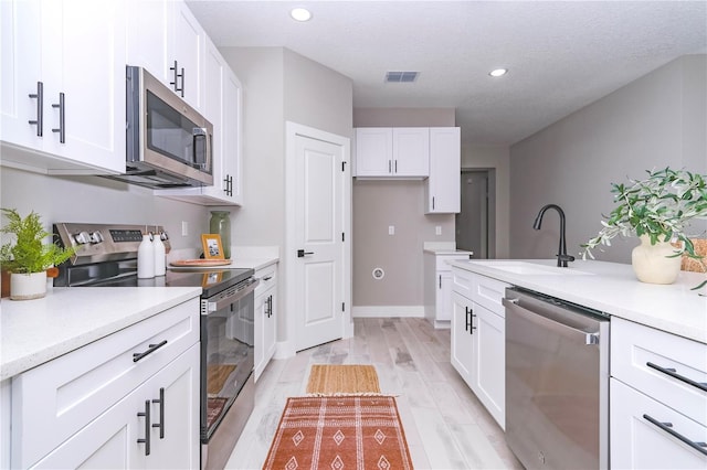 kitchen with white cabinets, sink, light wood-type flooring, a textured ceiling, and stainless steel appliances