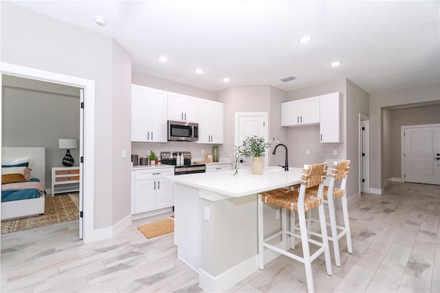 kitchen featuring a breakfast bar, white cabinets, an island with sink, appliances with stainless steel finishes, and light hardwood / wood-style floors