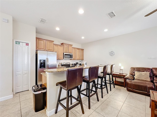 kitchen featuring ceiling fan, stainless steel appliances, light stone counters, a kitchen bar, and light tile patterned floors