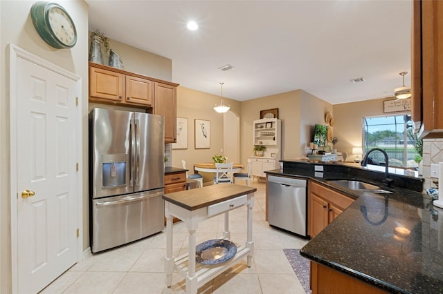 kitchen featuring sink, dark stone counters, pendant lighting, light tile patterned flooring, and appliances with stainless steel finishes