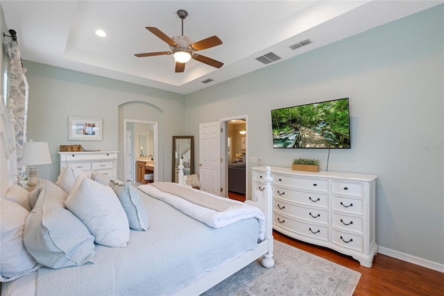 bedroom featuring a raised ceiling, ensuite bathroom, ceiling fan, and dark hardwood / wood-style flooring