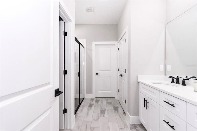 bathroom featuring vanity, wood-type flooring, a shower with shower door, and a textured ceiling