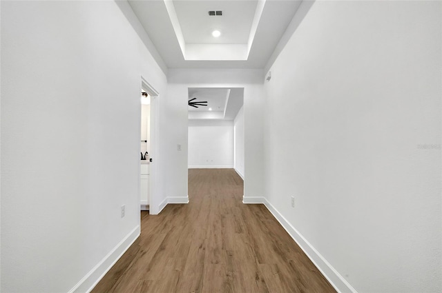 hall with a raised ceiling and light wood-type flooring