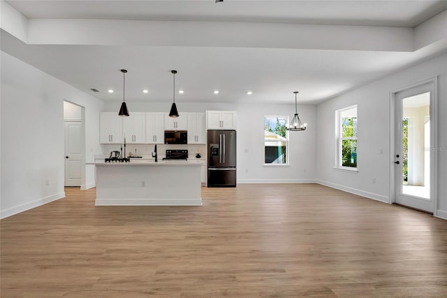 kitchen featuring black appliances, decorative light fixtures, light hardwood / wood-style flooring, white cabinetry, and an island with sink