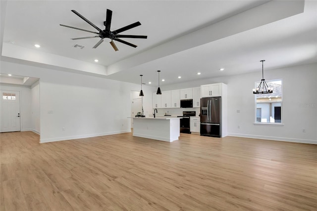 unfurnished living room featuring a wealth of natural light, sink, light hardwood / wood-style floors, and ceiling fan with notable chandelier