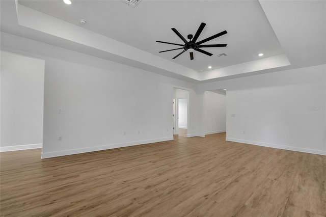 empty room with a raised ceiling, ceiling fan, and light hardwood / wood-style floors