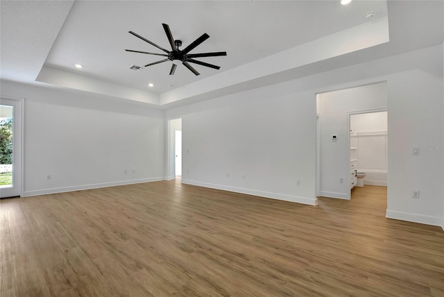 unfurnished living room featuring a raised ceiling, ceiling fan, and light hardwood / wood-style flooring