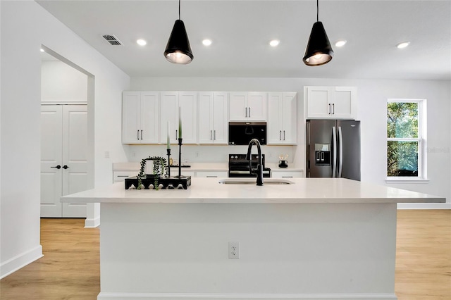 kitchen featuring decorative light fixtures, sink, appliances with stainless steel finishes, and an island with sink