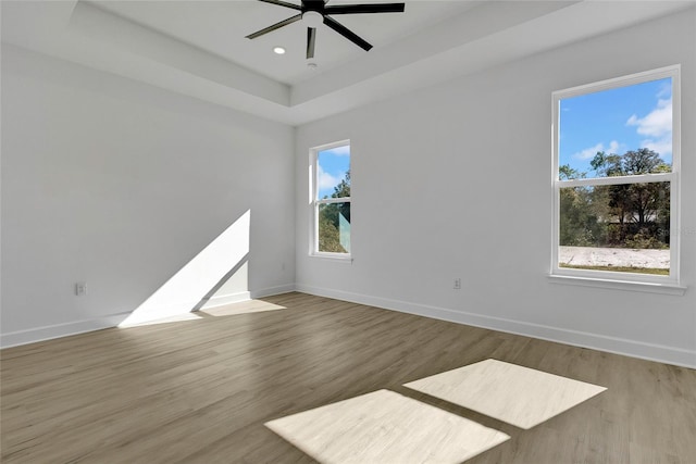 empty room featuring light hardwood / wood-style floors, ceiling fan, and a tray ceiling