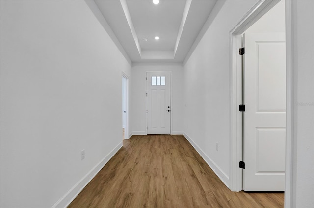 doorway with a tray ceiling and light hardwood / wood-style flooring