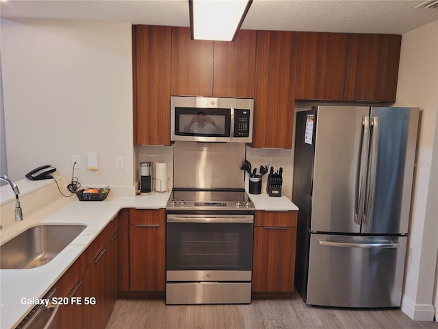 kitchen featuring a textured ceiling, light wood-type flooring, stainless steel appliances, and sink