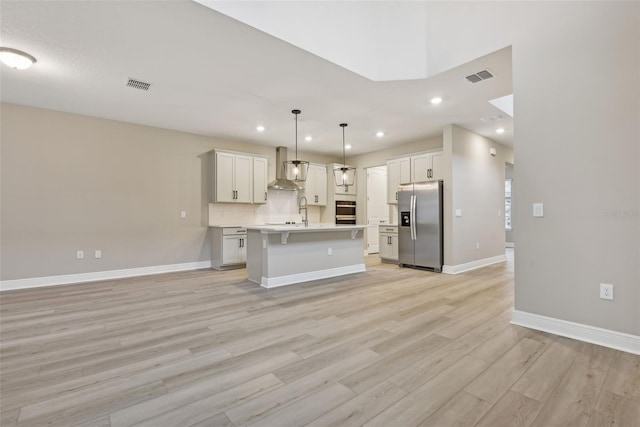 kitchen featuring appliances with stainless steel finishes, light hardwood / wood-style flooring, a kitchen island with sink, and pendant lighting