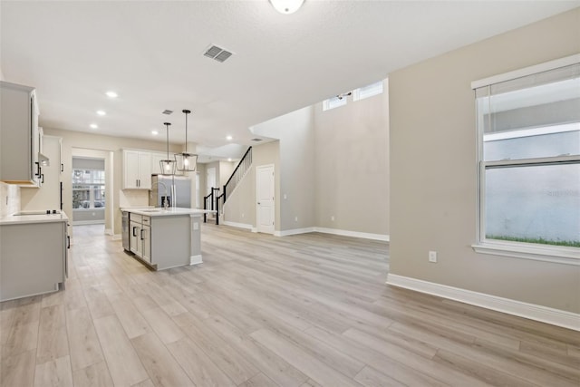 kitchen with stainless steel fridge, a center island with sink, decorative light fixtures, and light hardwood / wood-style flooring