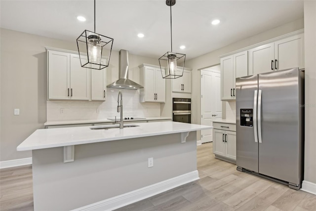 kitchen with stainless steel appliances, wall chimney range hood, pendant lighting, white cabinets, and light hardwood / wood-style floors