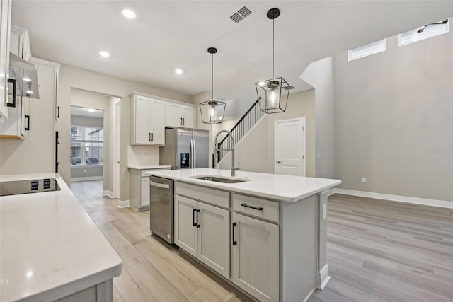 kitchen with stainless steel appliances, light hardwood / wood-style flooring, pendant lighting, a kitchen island with sink, and white cabinets