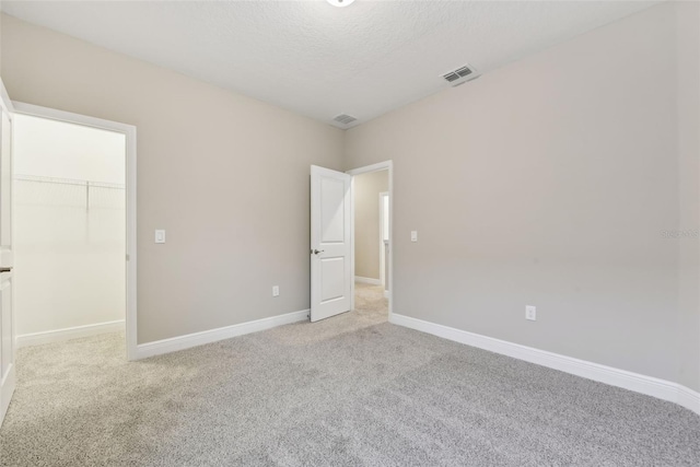 unfurnished bedroom featuring a textured ceiling, a spacious closet, light carpet, and a closet