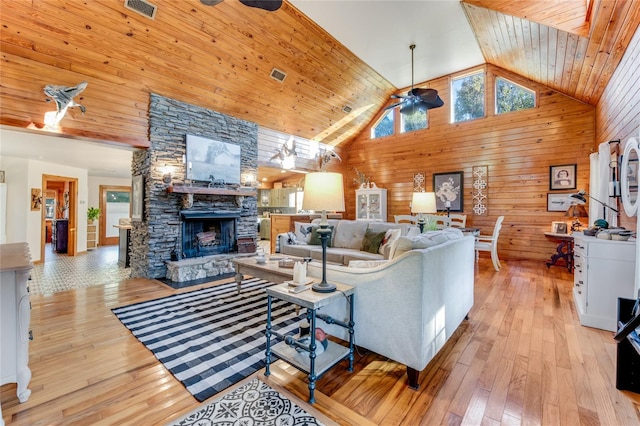 living room with light wood-type flooring, high vaulted ceiling, ceiling fan, and wood walls