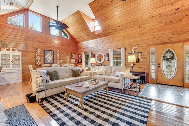 living room featuring light wood-type flooring, high vaulted ceiling, ceiling fan, and wood walls