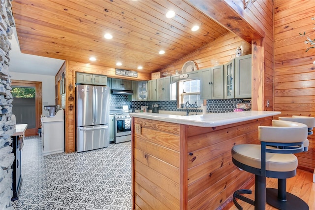 kitchen featuring stainless steel appliances, green cabinets, lofted ceiling with beams, kitchen peninsula, and wood walls