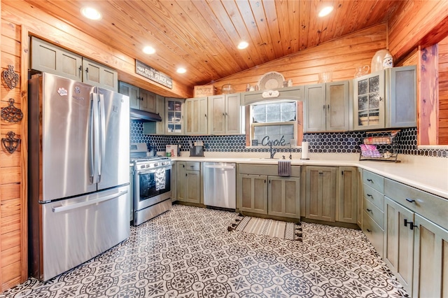 kitchen with appliances with stainless steel finishes, decorative light fixtures, vaulted ceiling, and wooden walls