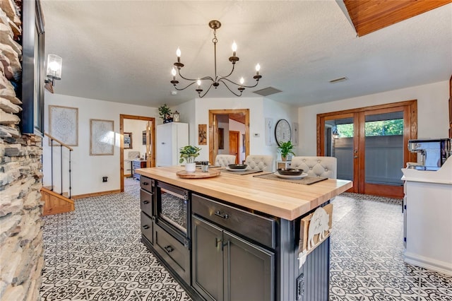 kitchen with a textured ceiling, stainless steel microwave, wooden counters, and decorative light fixtures