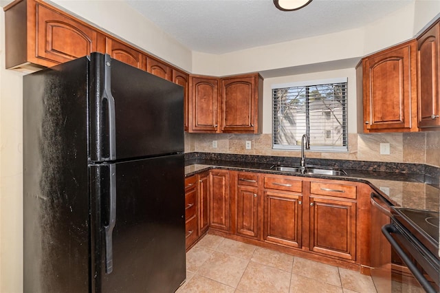 kitchen featuring sink, light tile patterned floors, black refrigerator, dark stone countertops, and backsplash