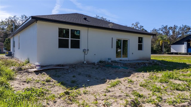 rear view of house with a shingled roof and stucco siding