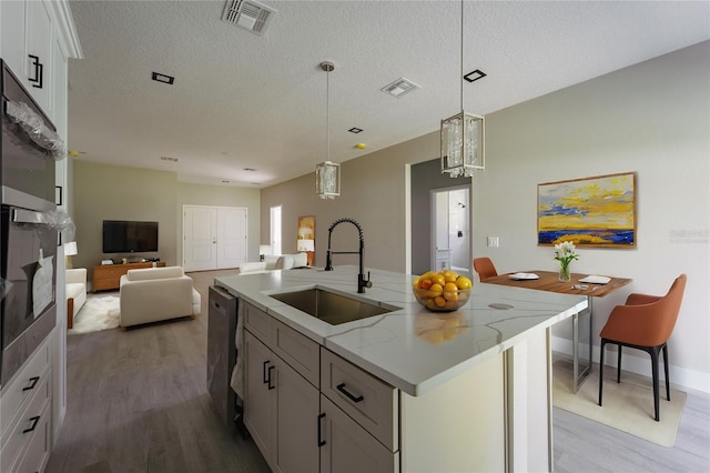 kitchen featuring visible vents, an island with sink, light stone counters, white cabinetry, and a sink