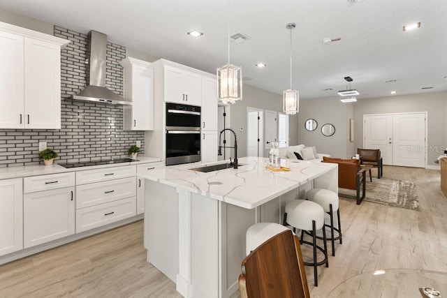 205 E 17th St, Apopka, FL 32703 - kitchen with wall chimney range hood, a sink, black electric stovetop, double oven, and light wood-style floors