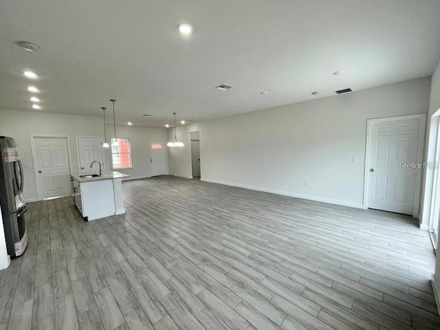 unfurnished living room with light hardwood / wood-style flooring, a notable chandelier, and sink