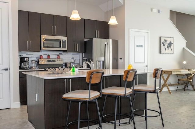 kitchen featuring dark brown cabinetry, a breakfast bar, hanging light fixtures, stainless steel appliances, and a center island with sink