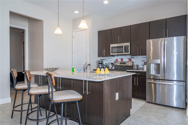 kitchen featuring decorative backsplash, appliances with stainless steel finishes, pendant lighting, a breakfast bar area, and an island with sink