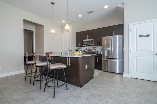 172 Villa Domani Cir, Davenport, FL 33896 - kitchen featuring stainless steel appliances, light countertops, a kitchen island with sink, a breakfast bar, and decorative backsplash