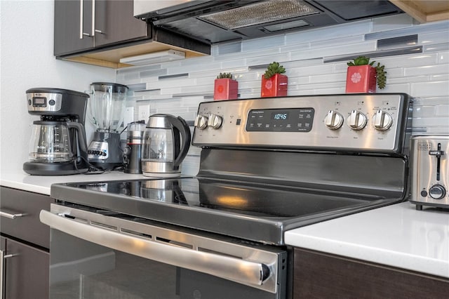 172 Villa Domani Cir, Davenport, FL 33896 - kitchen view of stainless steel range with electric stovetop, range hood, decorative backsplash, dark brown cabinetry, and light countertops